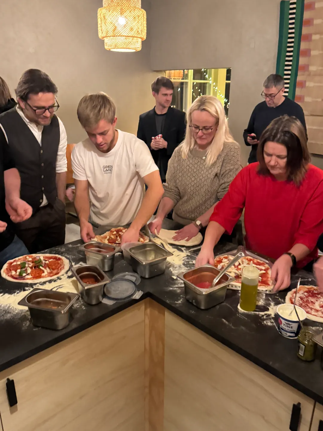 Kursdeltakere rundt en benk legger topping på hver sin pizzabunn