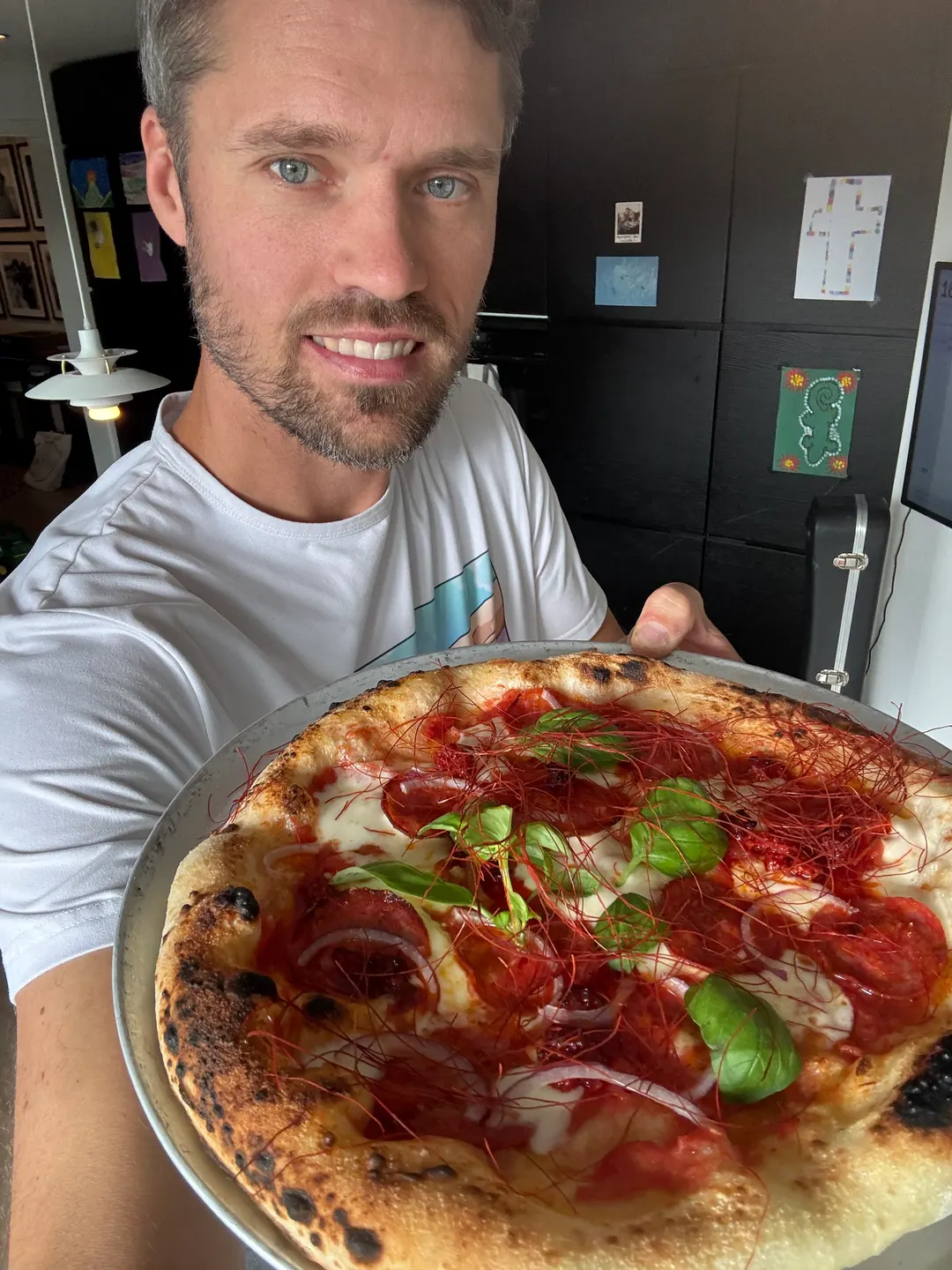 Vegard smiler og holder fram en nystekt pizza med chilitråder, basilikum og rødløk