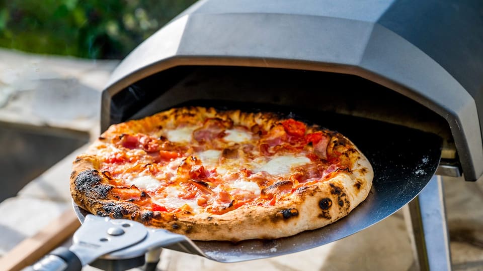 Nystekt pizza på spaden foran en bærbar pizzaovn utendørs