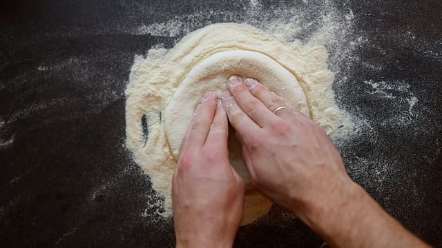 Hender som presser ut en pizzabunn i mel