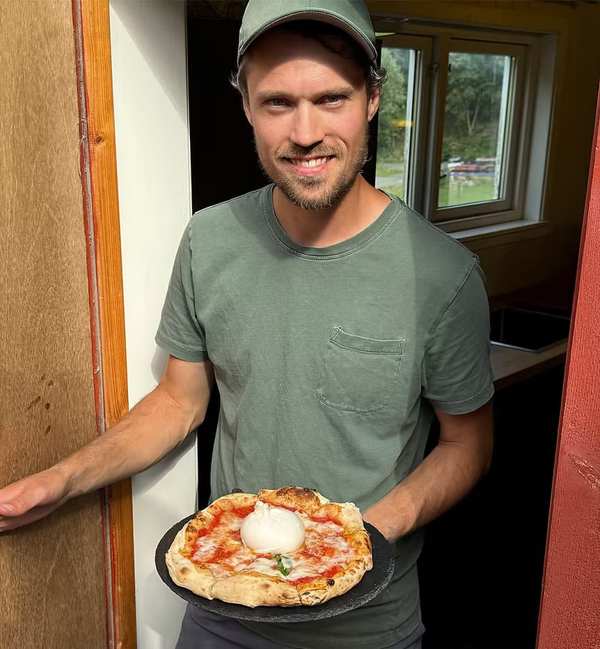 Vegard smiler og holder en nystekt pizza med burrata